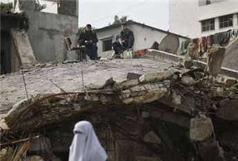 A woman walks past as policemen sit atop their destroyed headquarters in Gaza City, Nov. 25.
