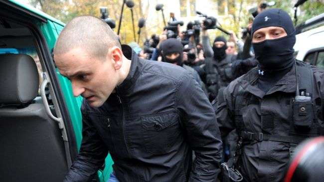 Ultra-left opposition leader Sergei Udaltsov gets into a vehicle as masked Interior Ministry officers take him in for questioning after the search of his home in Moscow, October 17, 2012.