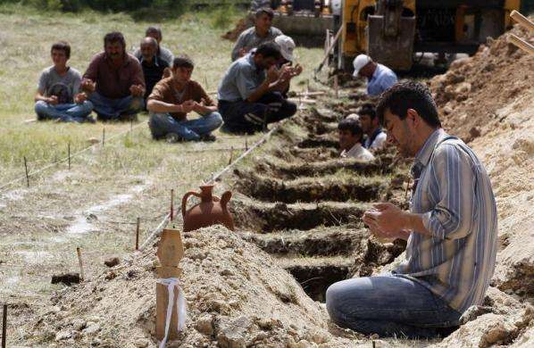 A man prays beside a grave of a dead miner while workers dig graves and locals accompany the praying in a cemetary in Soma, a district in Turkey western province of Manisa May 14, 2014.