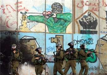 Israeli soldiers stand in front of the graffiti covered separation barrier during clashes with Palestinians at the Qalandia checkpoint between Ramallah and Jerusalem on Aug. 13, 2014