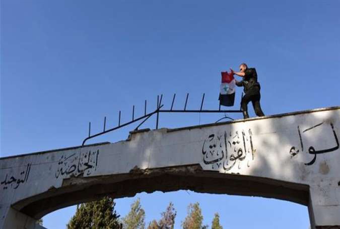 A Syrian soldier raises the national flag over the entrance to the al-Figeh Village in the Wadi Barada area in Damascus’ countryside, January 28, 2017.