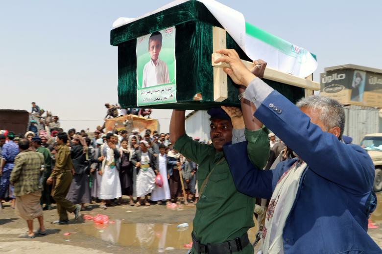 A mourner and a policeman carry the coffin of a boy during the funeral of people, mainly children, killed in a Saudi-led coalition air strike on a bus in northern Yemen, in Saada.