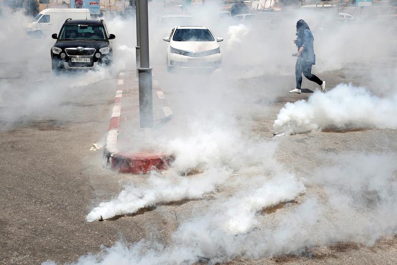 A Palestinian woman photographer runs away from tear gas fired by Israeli forces during a protest against a two-day international meeting in Bahrain for the Trump administration's Israeli-Palestinian peace plan, near the Jewish settlement of Beit El, in 