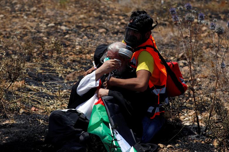A Palestinian paramedic tends to a clergyman after inhaling tear gas fired by Israeli forces during a protest against Bahrain's workshop for U.S. peace plan, near the Jewish settlement of Beit El, in the Israeli-occupied West Bank June 25