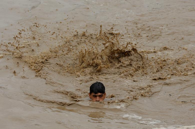 A man swims in flood waters while heading for a higher ground, following rains and floods during the monsoon season in Charsadda, Pakistan August 27, 2022.